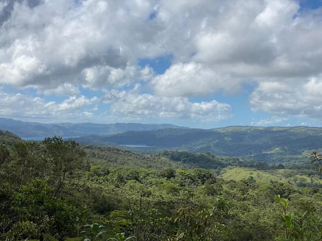 Una vista de un valle verde con montañas al fondo y un cielo azul con nubes blancas. Una vista de un valle verde con montañas al fondo y un cielo azul con nubes blancas.