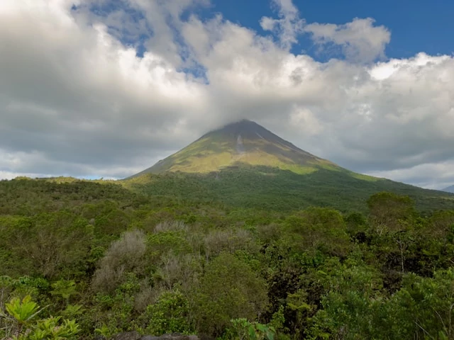 Un volcán muy alto y grande rodeado de plantas verdes y vegetación con un cielo azul cubierto de nubes blancas. Un volcán muy alto y grande rodeado de plantas verdes y vegetación con un cielo azul cubierto de nubes blancas.