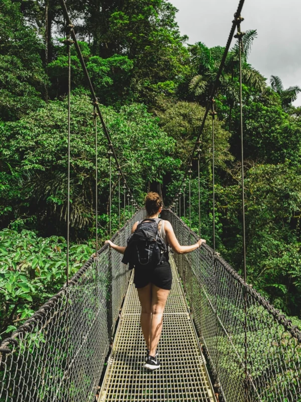 Una mujer cruzando un puente colgante en medio de la jungla.