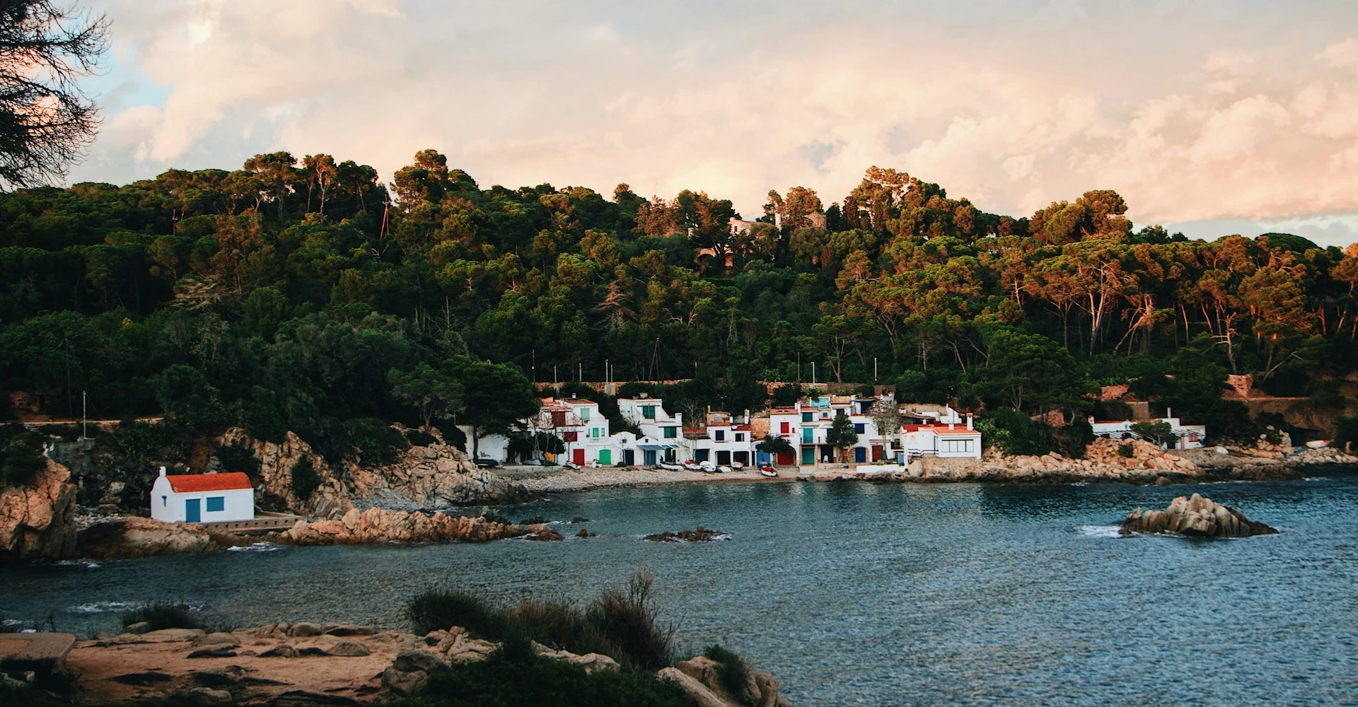 The small cove of Cala s'Alguer famous for it's white fishing houses, right next to a pine forest during a sunset.
