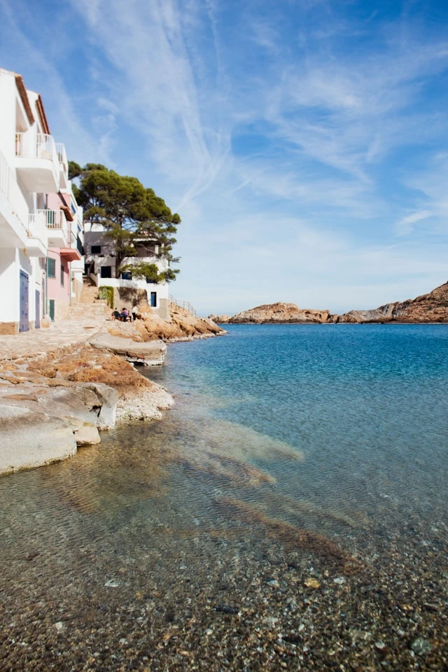 The quiet beach of Sa Tuna, with its white and colorful houses, and the coastal path leading up to the pine forests