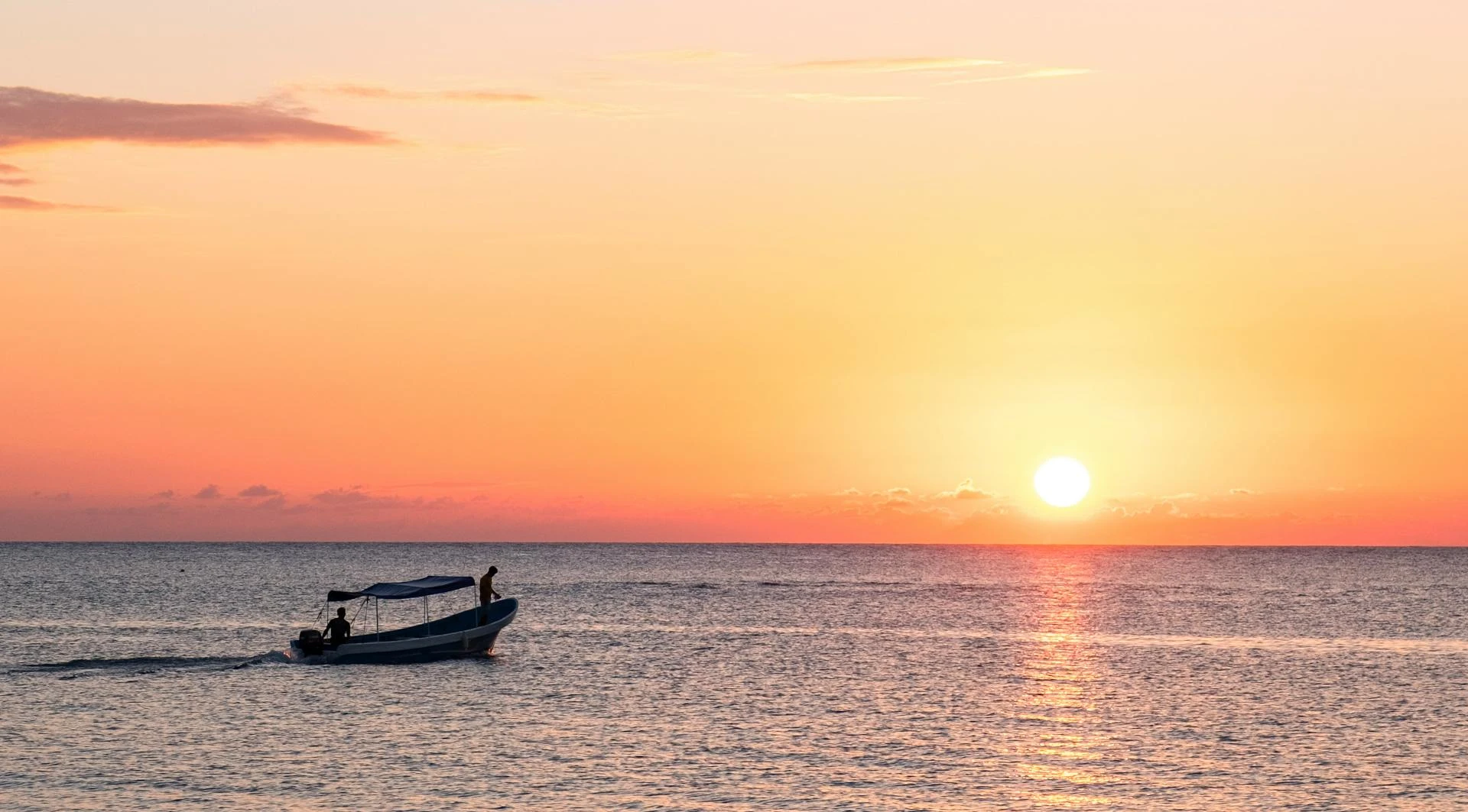 A beautiful sunset with an orange and purple sky, and some people sailing a boat in the Caribbean Sea.