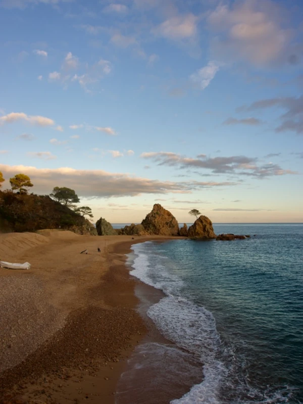 A beach of golden sands and rocks jutting out into the sea at the end.