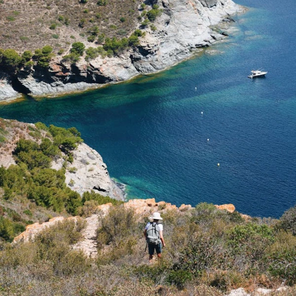 Person hiking in an arid natural area, overlooking the sea with its blue waters