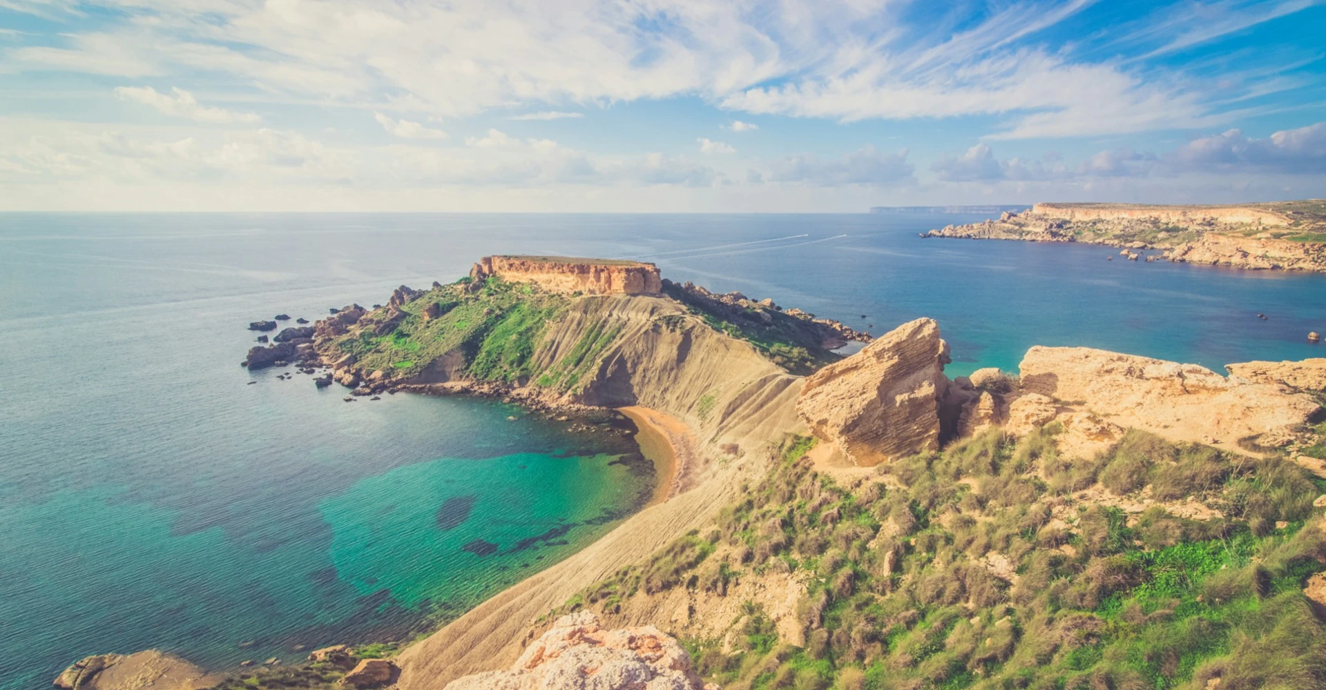 Qarraba Bay’s striking clay cliffs with green vegetation contrasting against the calm, clear blue sea in Malta