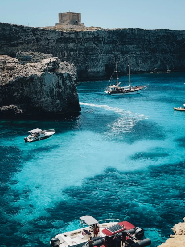 Boats sailing in the turquoise waters of Comino with Santa Marija Tower in the distance.