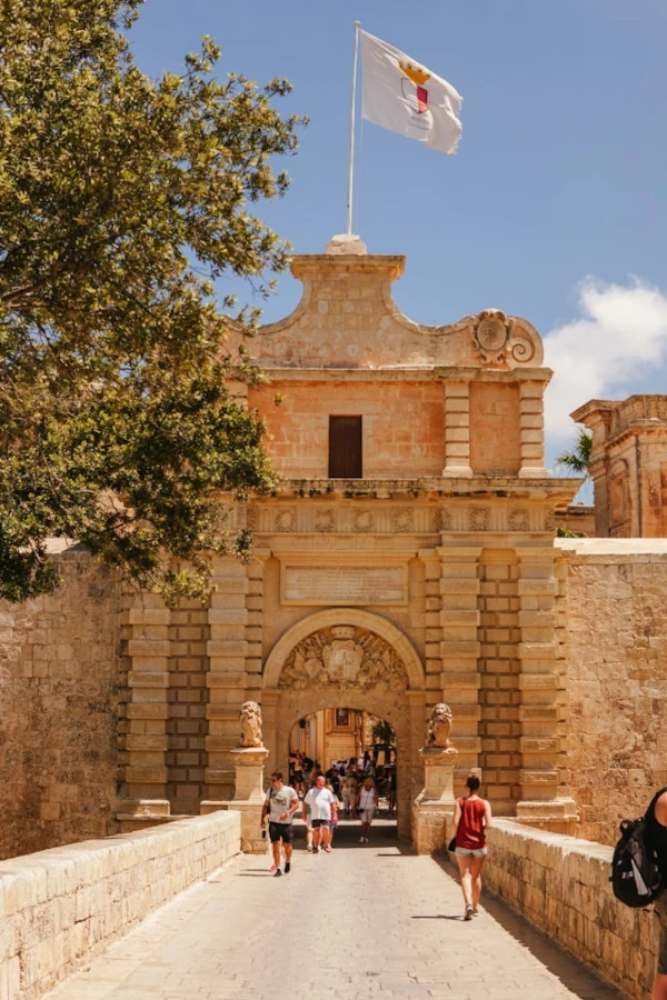 La puerta principal de Mdina en Malta en un día soleado, con turistas caminando por la entrada histórica.