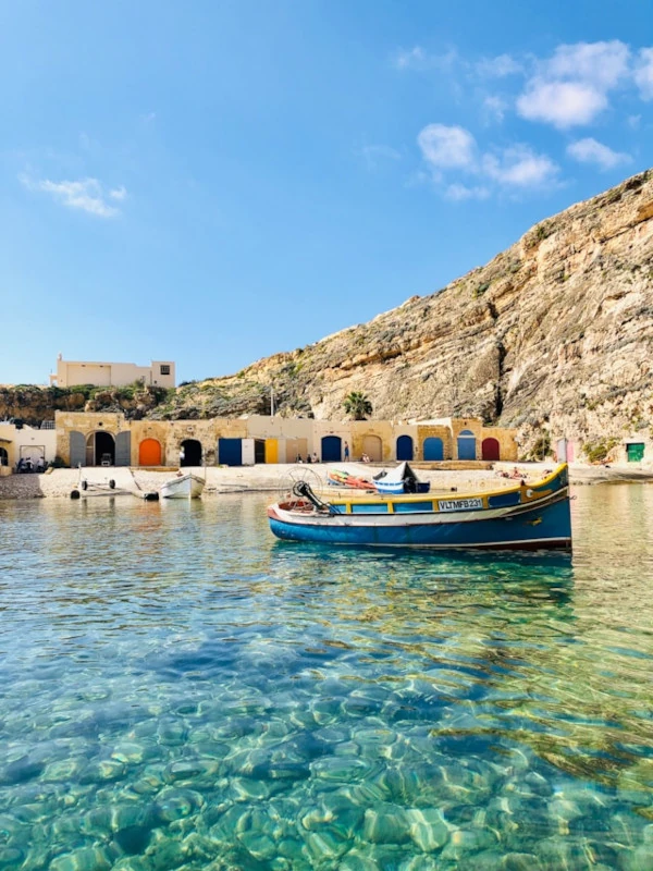Tranquilas aguas turquesas del Mar Interior de Gozo con un barco pesquero azul y edificios coloridos detrás.