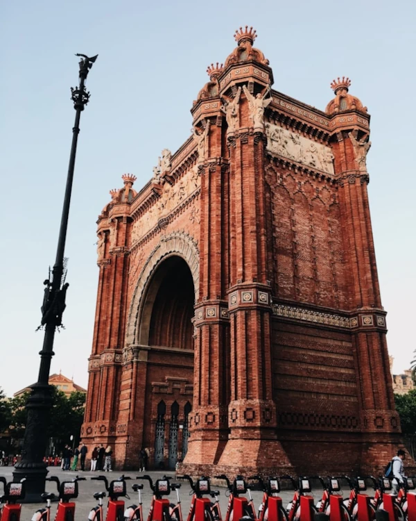 The Arc de Triomf in Barcelona with a lot of red bicycles parked in front of it on a clear sunny day