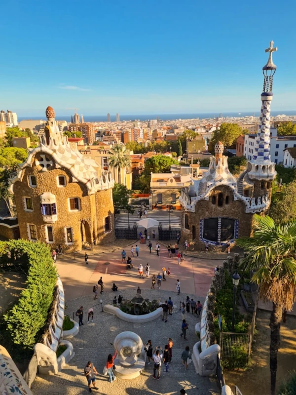A lively group of people stroll through Park Güell in Barcelona, Spain, weaving past Gaudí’s iconic ceramic benches and whimsical architecture.