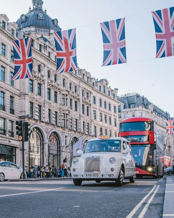 A classic London taxi and red double-decked red bus behind, with UK flags hanging from the street