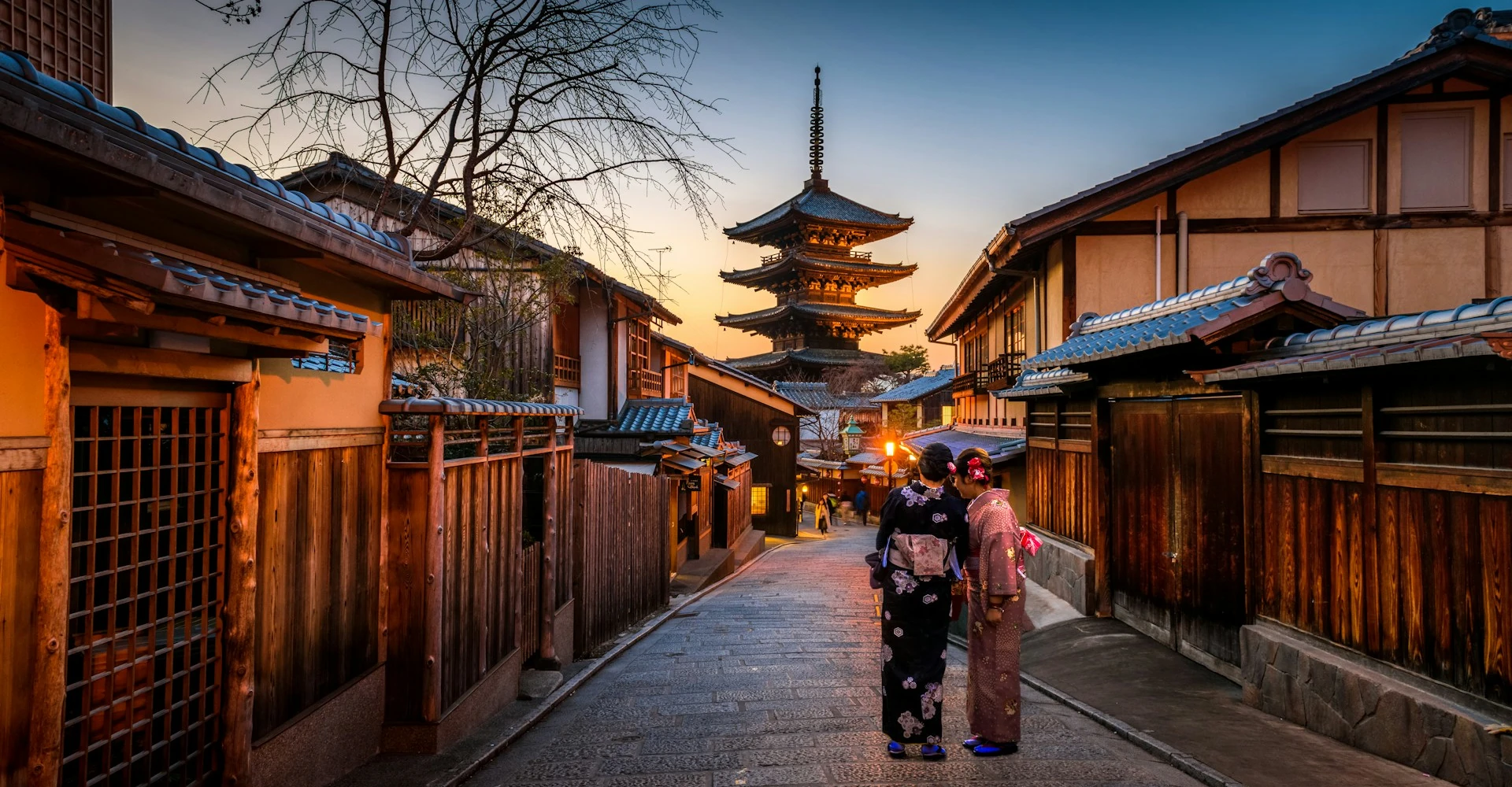 Two women in purple and pink kimono standing on a street in Kyoto