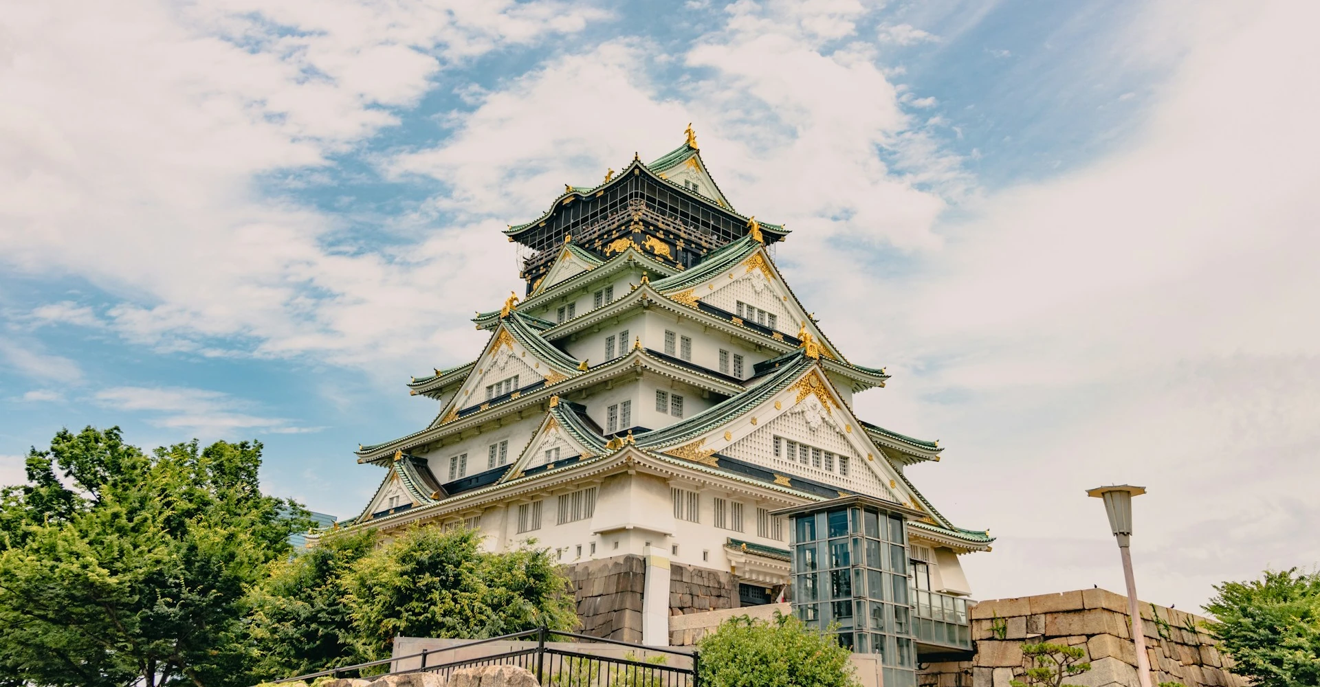Scenic view of Osaka Castle surrounded by lush greenery on a cloudy spring day.