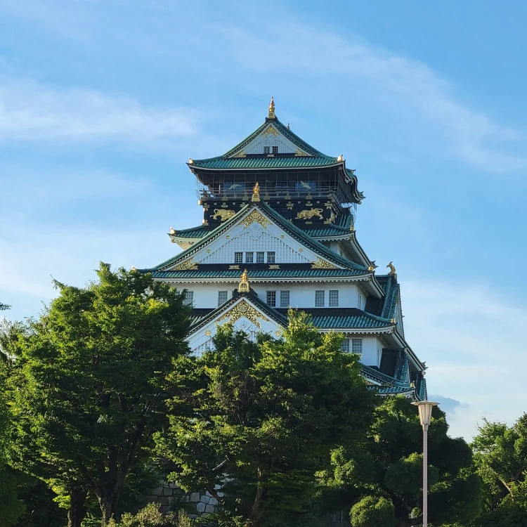 Iconic Osaka Castle stands majestically against a bright blue sky, surrounded by lush greenery.