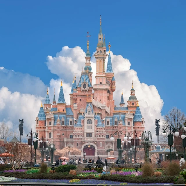 The iconic Disney castle, with people taking photos, and a big white cloud in the distance