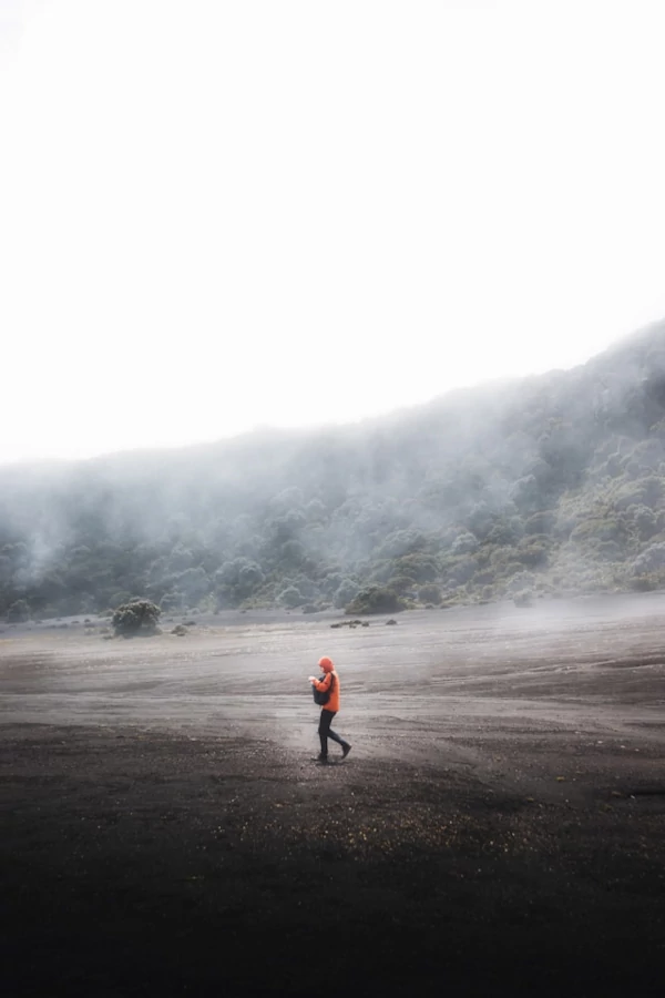 Qué hacer en el Parque Nacional Volcán Irazú Un hombre con una chaqueta naranja caminando por terreno volcánico.